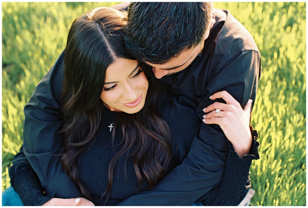 man and woman sitting and embracing in green grass field dutton ranch inspired engagement photos