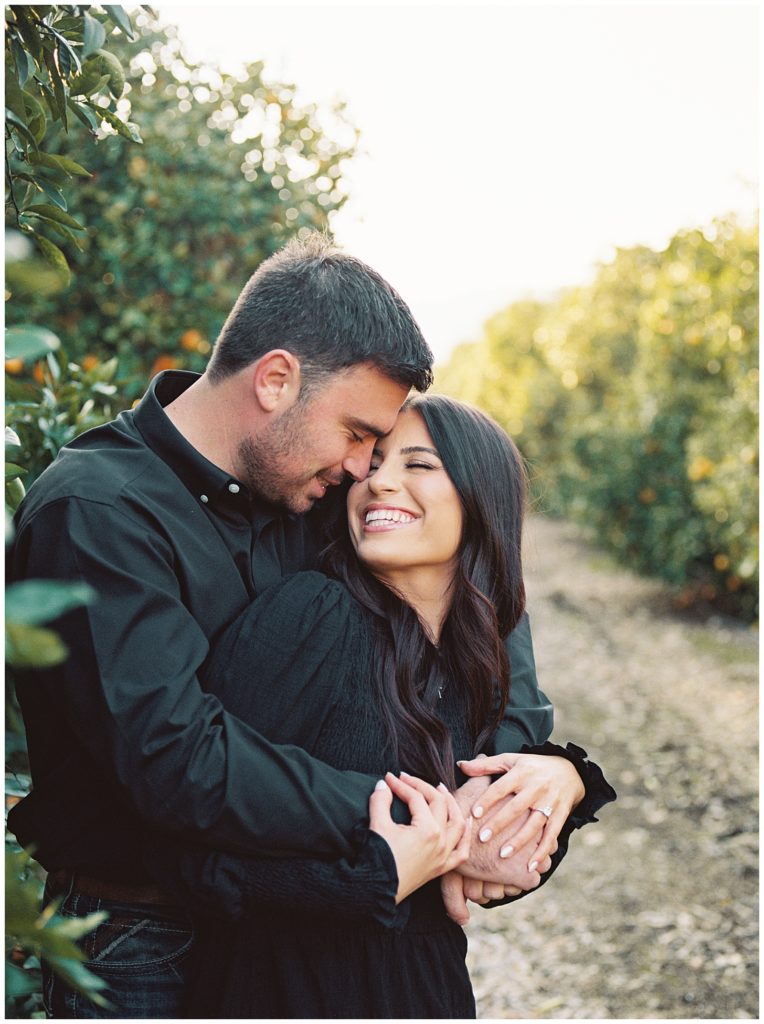man hugging fiance smiling in orange grove dutton ranch inspired engagement photos