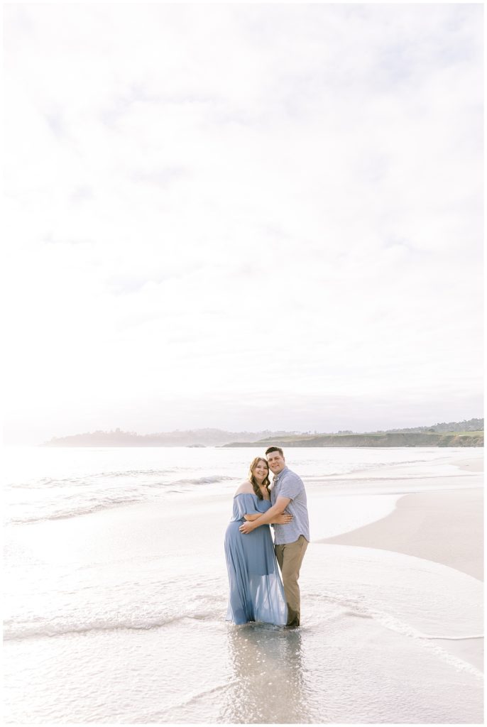 engaged couple standing on beach smiling