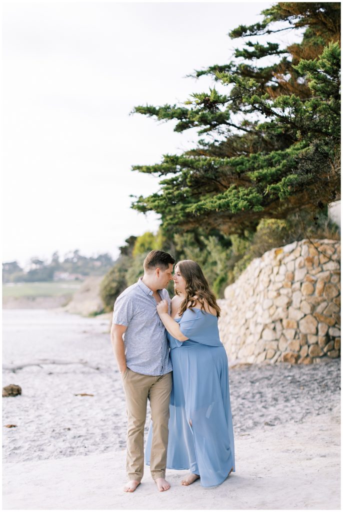 engaged couple hugging standing on beach wearing blue